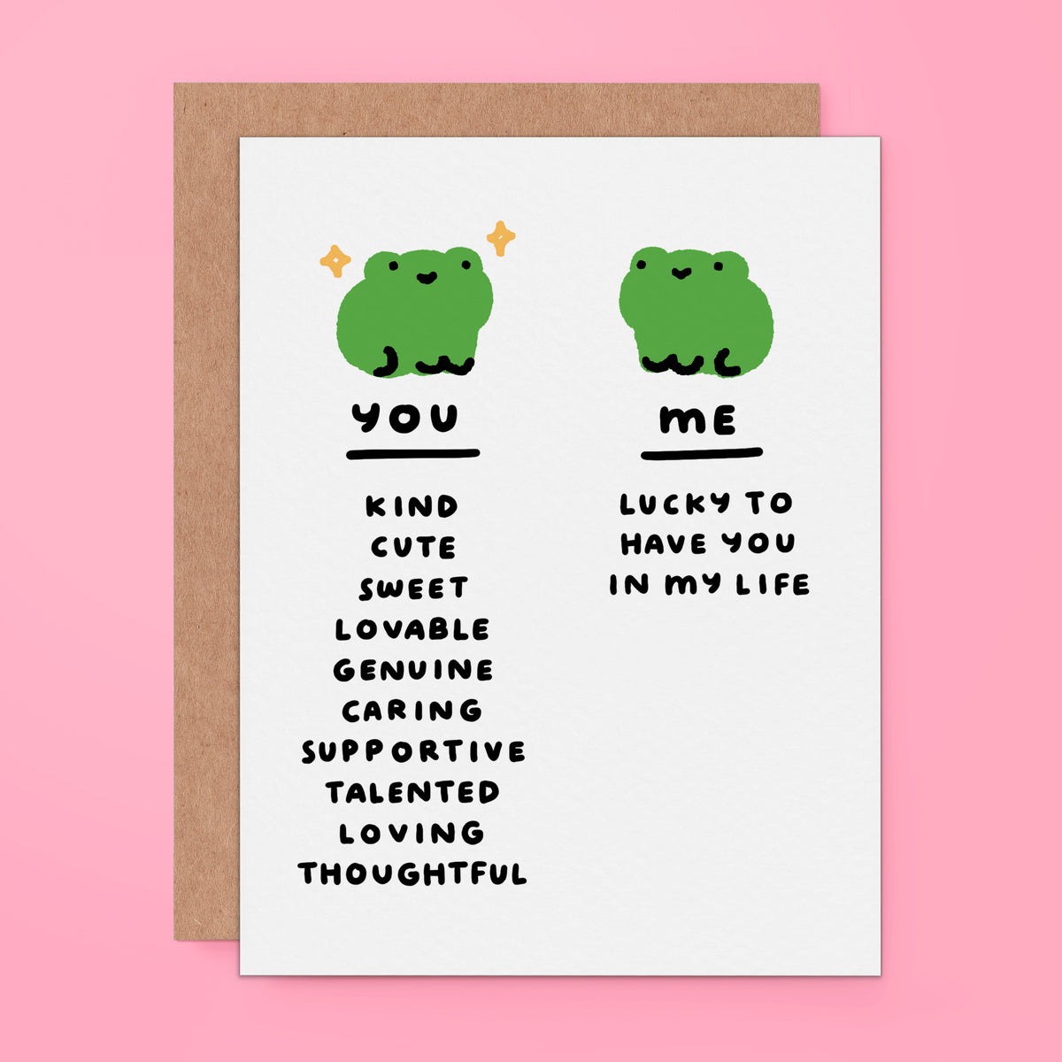 A white greeting card with a brown kraft envelope behind it, featuring two green cartoon frogs and text comparing qualities of 'you' and 'me' on a pink background.